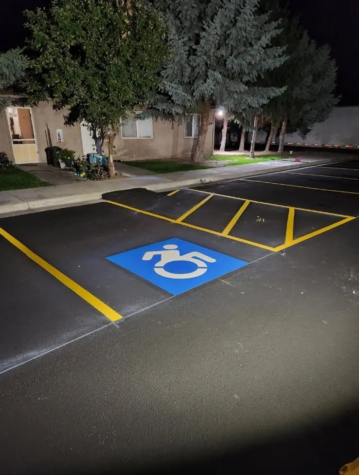Fresh yellow stall lines, a hatched aisle and a blue accessible parking symbol on an apartment lot at night