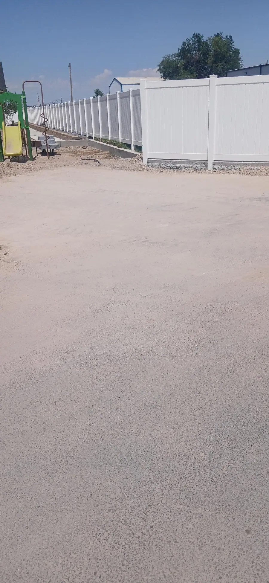 A swept lot beside new white vinyl fencing at a construction site
